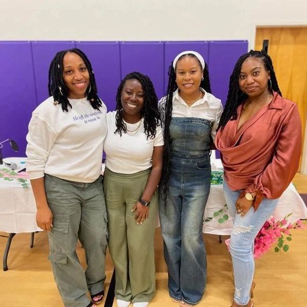 Four women smiling and standing together in a gymnasium.