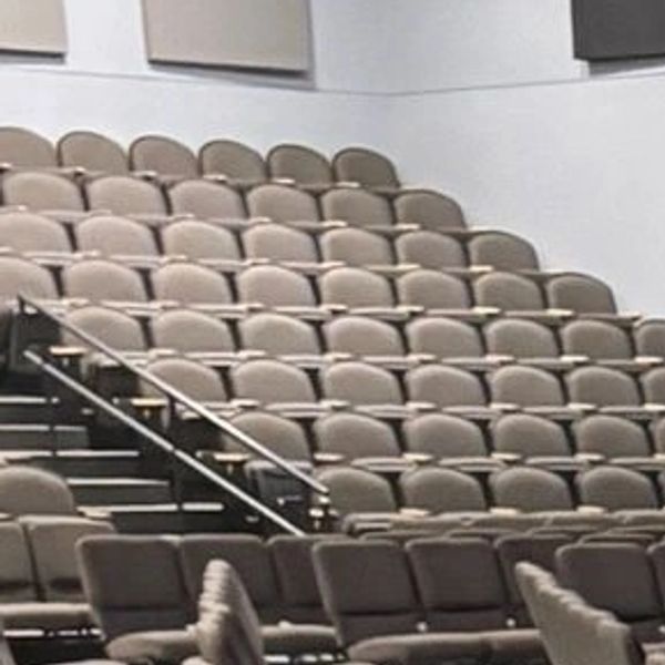 Empty tiered lecture hall seating with beige chairs and stair railings.
