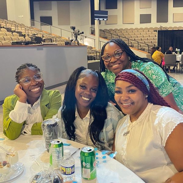 Four women smiling around a table at an indoor event.