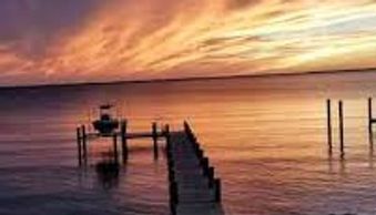 A wooden pier extends into calm water under a colorful sunset sky.