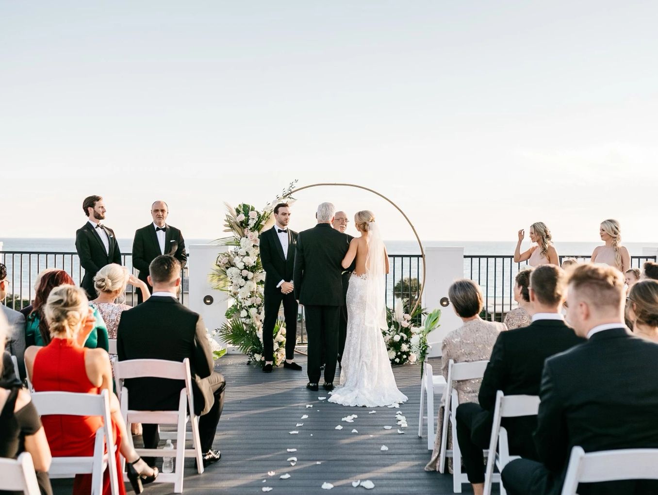 Outdoor wedding ceremony by the sea with guests seated.