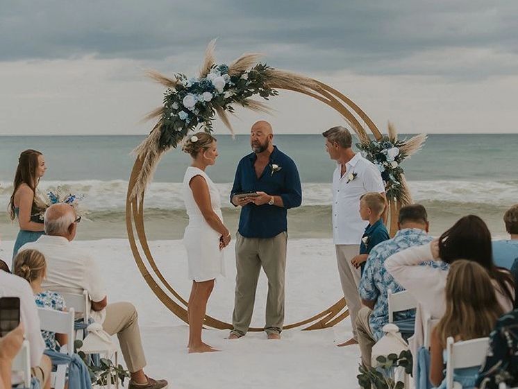 Beach wedding ceremony with couple and officiant.