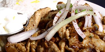 Grilled meat skewers with green garnish and sauce on a white plate.