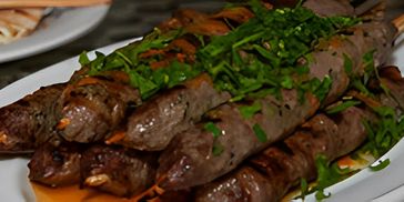 Close-up of sliced meat and onions with a side of white sauce.