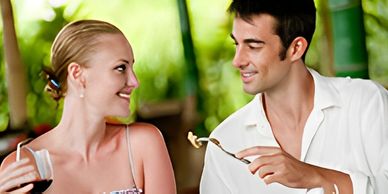 Hand pouring olive oil from a bottle onto a wooden spoon.