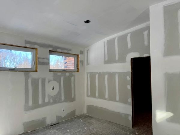 A room under construction with drywall installed and two small windows.