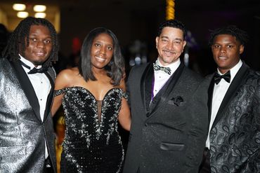 Four people dressed elegantly in black and silver formal wear at an event.