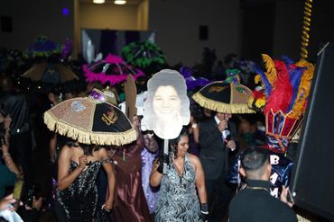 People dancing with decorative umbrellas and a large face cutout at a vibrant indoor event.