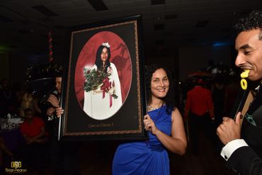 Woman in blue dress holding a framed portrait of Queen Elaine I at an event.