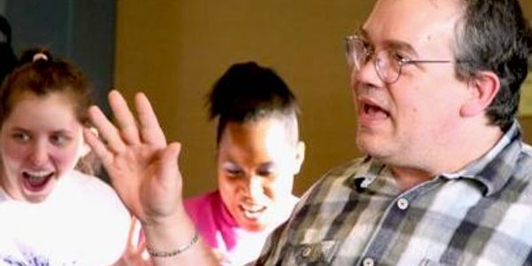 A man passionately talks while two young people react excitedly.