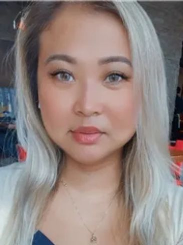 A woman with long blonde hair wearing a navy blue top and white cardigan.