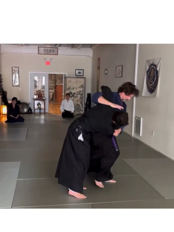Two martial artists practice a grappling technique in a dojo.