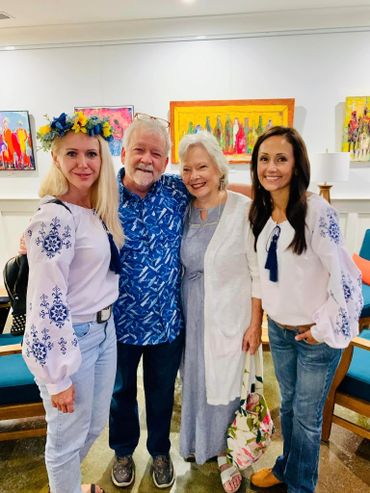 Four smiling people posing indoors with colorful paintings in the background.
