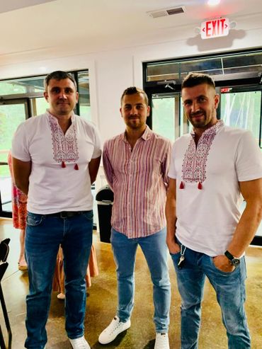 Three men posing indoors, two wearing embroidered white shirts and one in a striped shirt.