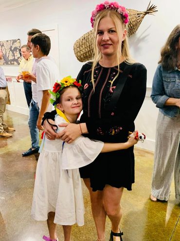 A woman and child wearing floral crowns hug at a social gathering indoors.