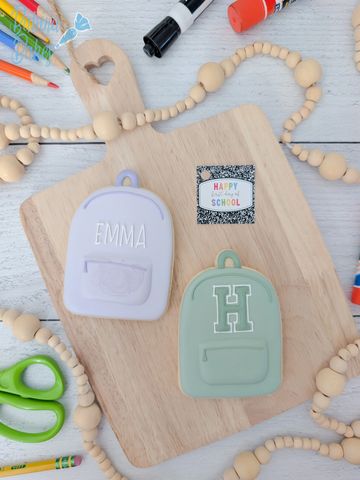 Two small backpack-shaped items on a wooden board with art supplies.