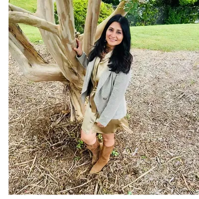 Woman standing by a tree, smiling at the camera.