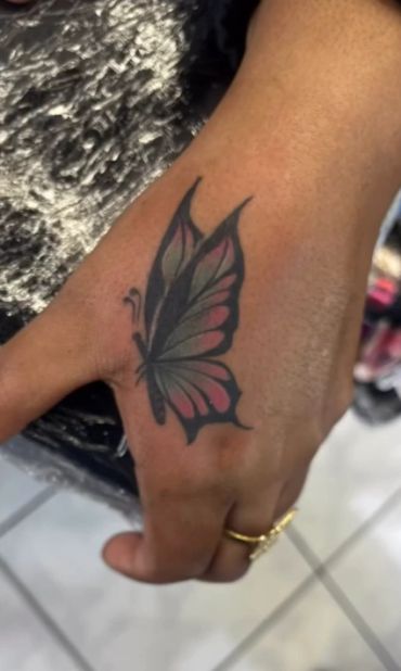Butterfly tattoo on hand with pink and black wings.