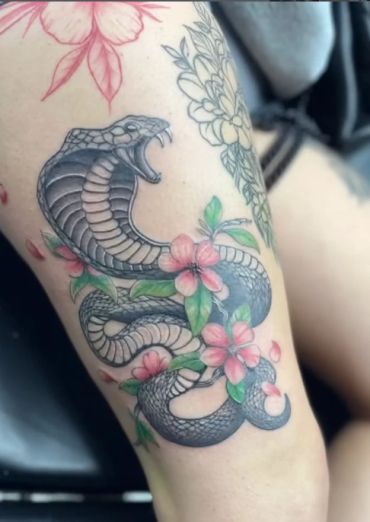 Tattoo of a roaring snake with pink flowers.