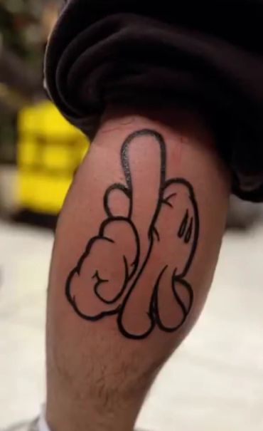 Tattoo of a cartoon hand giving the middle finger on a leg.