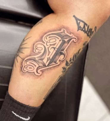 Tattoo of a stylized letter F on a person's leg.
