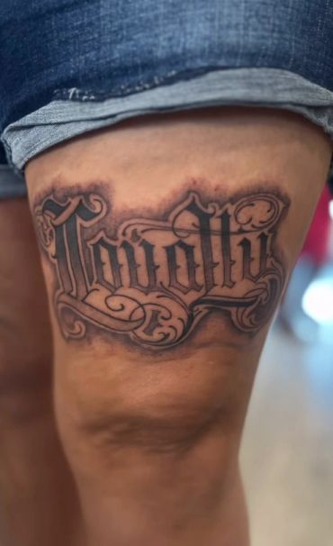 Tattoo with the word 'Loyalty' on a thigh.