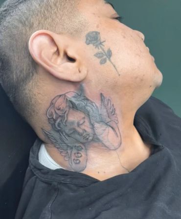 Person with detailed angel and rose tattoos on neck and face.
