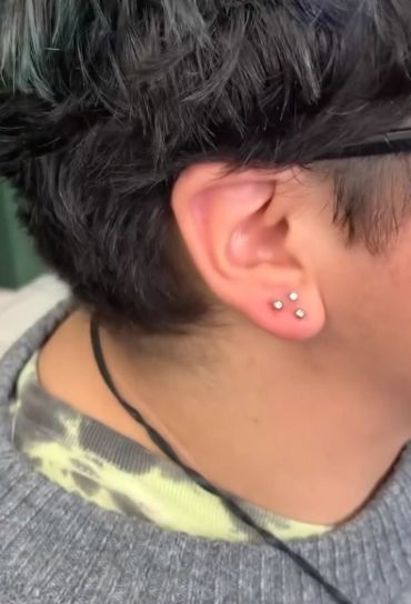 Close-up of ear with three small diamond earrings.
