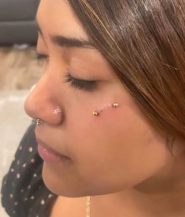 Close-up of a woman's face with cheek piercings.