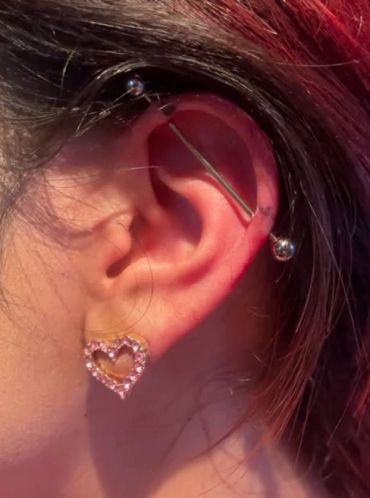 Ear with industrial piercing and heart-shaped earring.