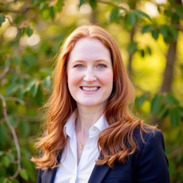 Professional woman with red hair smiling outdoors in business attire.