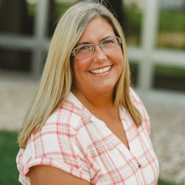 Smiling woman with glasses and long blonde hair outdoors.