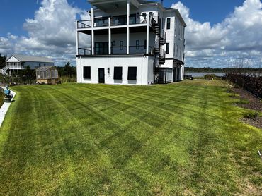 Large modern white house with manicured lawn and lake view.