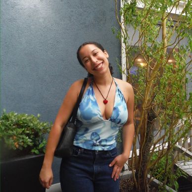 Smiling woman posing outdoors with plants in background.