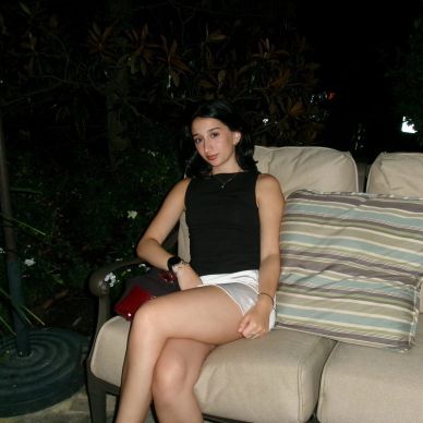 Young woman sitting on an outdoor cushioned chair at night.