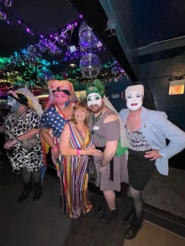 Group of people in colorful and theatrical costumes at a lively party with disco lights.