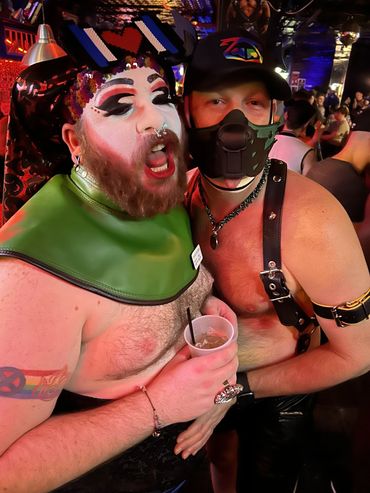 Two men dressed in bold, expressive outfits at a lively nighttime event.