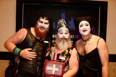 Three men in theatrical makeup and costumes pose together indoors.