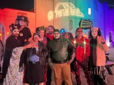 Group of people in colorful costumes posing at night with illuminated building.