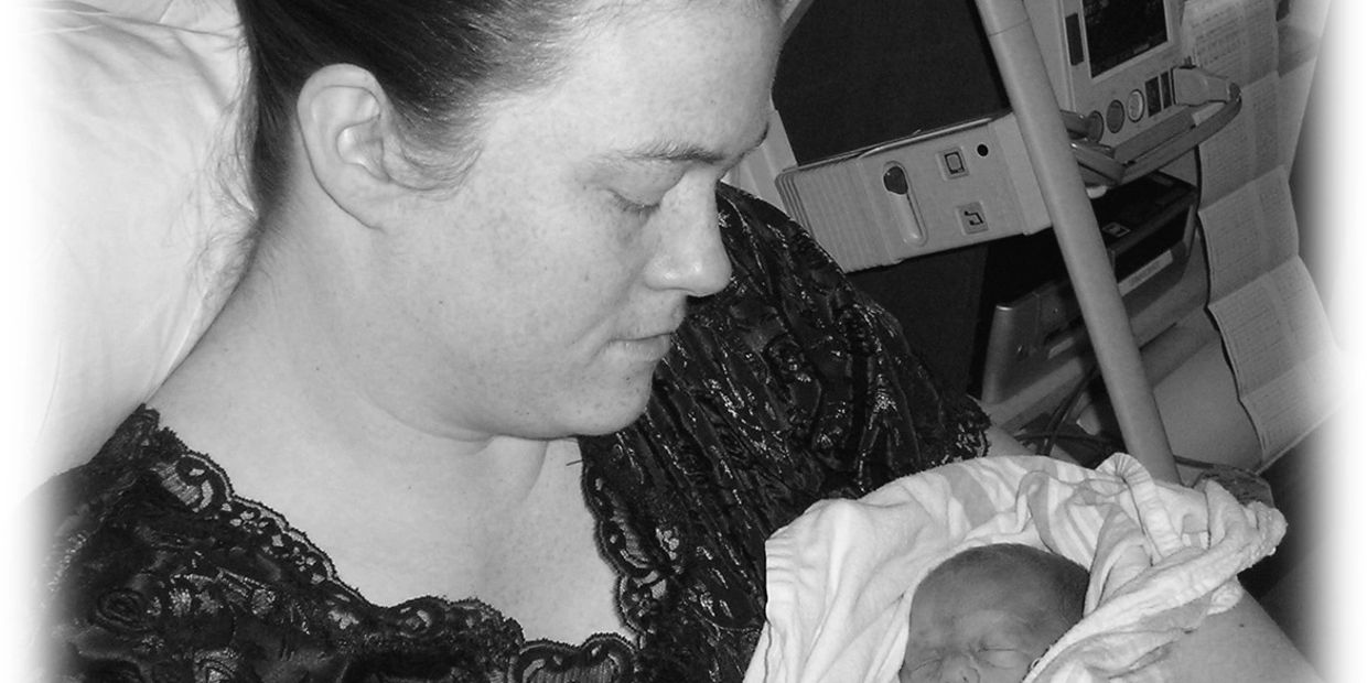 Black and white photo of a woman holding her baby. She is wearing a dark nightgown and her hair is p