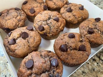 A box of freshly baked chocolate chip muffins on a kitchen counter.