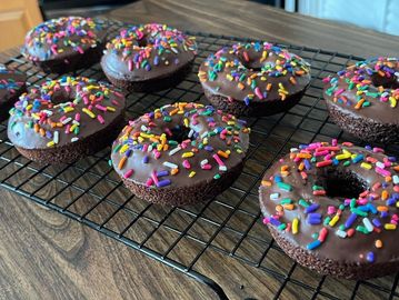 Chocolate donuts with colorful sprinkles cooling on a wire rack.