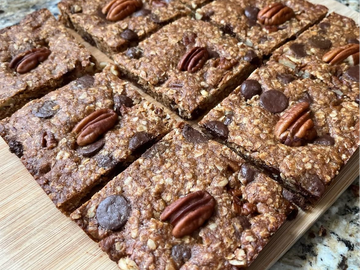 Homemade oat and chocolate chip bars topped with pecans on a wooden board.