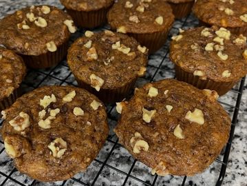 Freshly baked muffins topped with chopped nuts cooling on a wire rack.