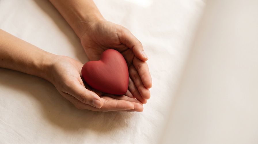 Two small hands cradle a red heart-shaped figure, a quiet symbol of hope offered and held.