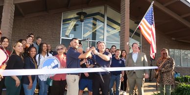 Group cutting ribbon at event with American flag.