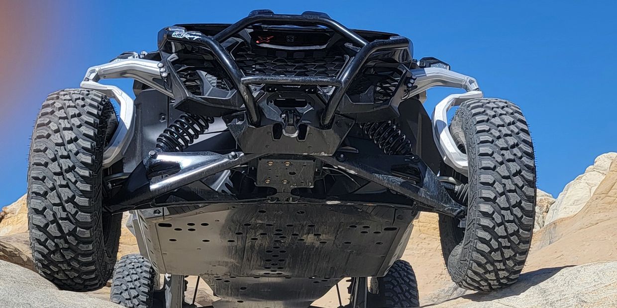 Off-road vehicle climbing rocky terrain under clear blue sky.