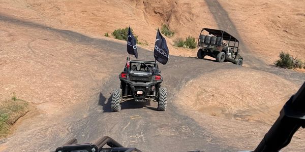 Off-road vehicles climbing rocky terrain under clear blue sky.
