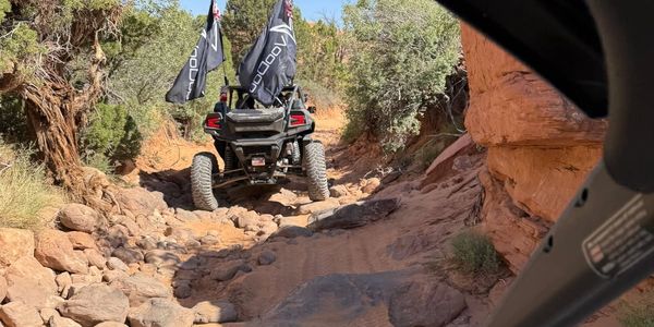 Two off-road vehicles navigating a rocky desert trail under a clear blue sky.
