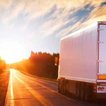 A large white truck driving on a road at sunset with a glowing sky.